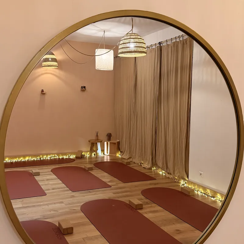 Miroir rond à cadre doré reflétant des suspensions en fibres naturelles, des rideaux beiges et des tapis terracotta.