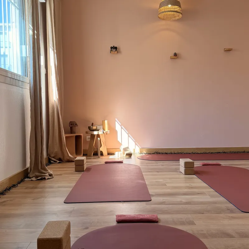 Salle baignée de lumière près d'une grande fenêtre aux rideaux beiges, avec un tapis terracotta au premier plan et des briques en liège au fond.