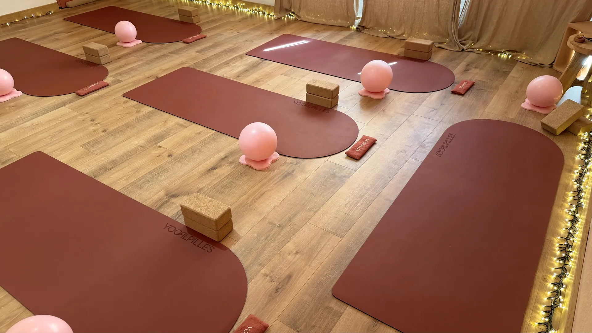 Salle du studio Yogalpilles avec des tapis de yoga terracotta, des briques en liège, des ballons de Pilates et des guirlandes lumineuses.