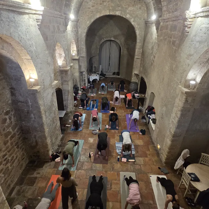 Cours de yoga collectif dans une chapelle en pierre voûtée, vu d’en haut