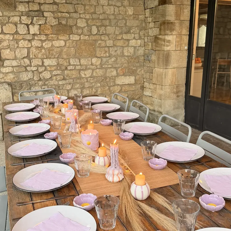 Longue table dressée avec assiettes roses et décoration naturelle devant un mur en pierre