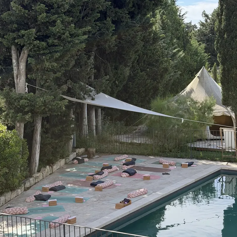 Tapis de yoga alignés au bord d’une piscine, sous les arbres et une voile d’ombrage