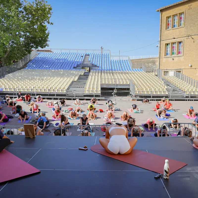 Cours de yoga collectif sur une grande scène en plein air face aux gradins