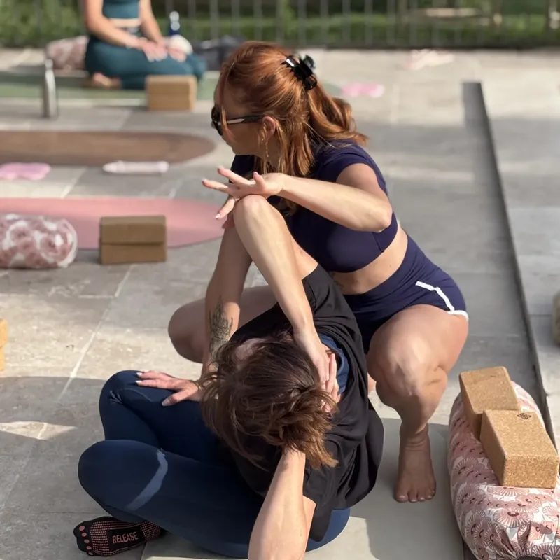 Professeure corrigeant la posture d’une élève assise lors d’un cours de yoga en extérieur