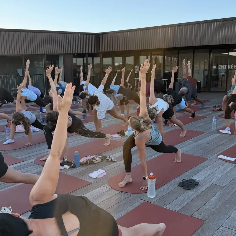 Élèves en fente basse, bras levés, sur des tapis terracotta installés sur une terrasse en bois