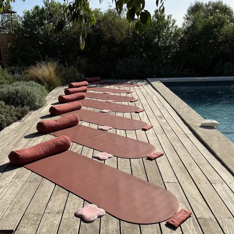 Tapis de yoga terracotta roulés et alignés sur une terrasse en bois au bord de la piscine