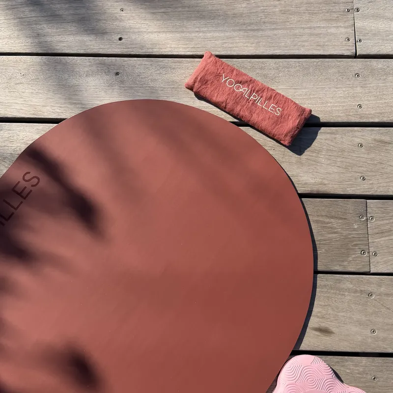 Tapis de yoga rond terracotta et petit coussin posés sur un plancher en bois