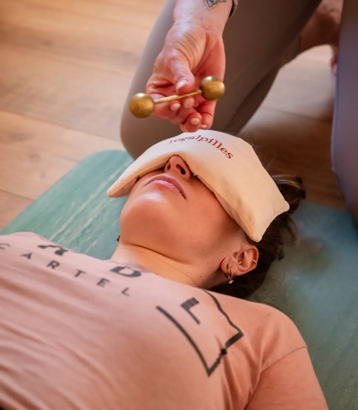 Femme allongée en relaxation, coussin pour les yeux Yogalpilles sur le visage, une main tenant un outil doré au-dessus d'elle