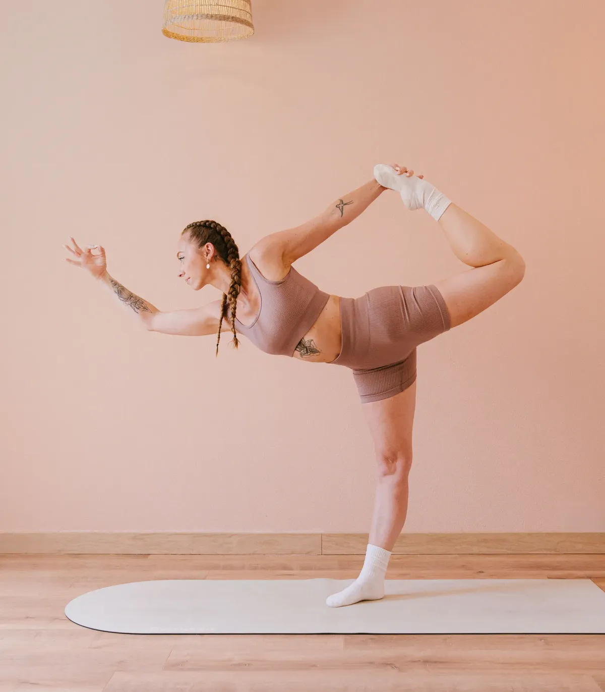 Charlotte en posture du danseur, en équilibre sur une jambe, la main tenant son pied derrière elle, sur un tapis de yoga clair